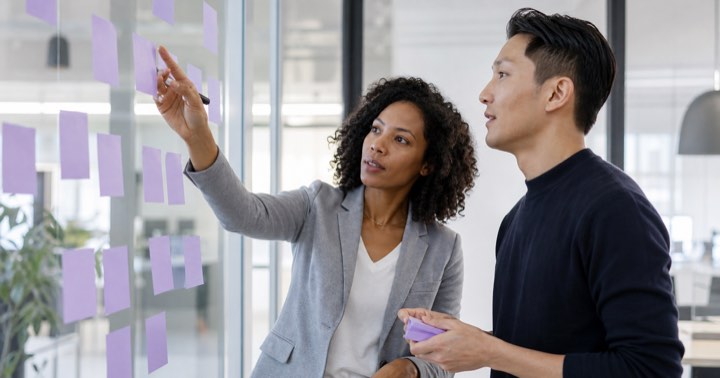 Two colleagues planning at a glass wall covered in sticky notes