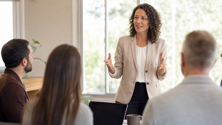 A team lead presenting to a small seated group in a meeting room
